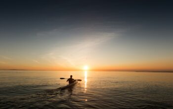 man riding kayak on water taken at sunset